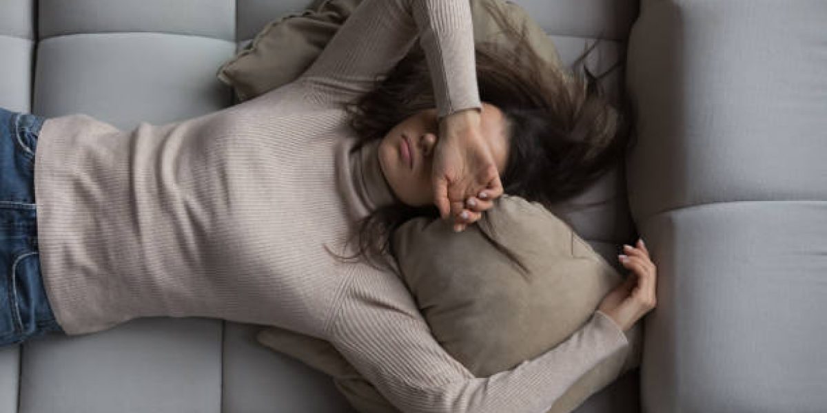 Peaceful pretty 20s girl lying on back on comfortable couch at home, covering eyes with hand, sleeping at daytime, feeling tired, enjoying relaxation, leisure, break, weekend. Top view
